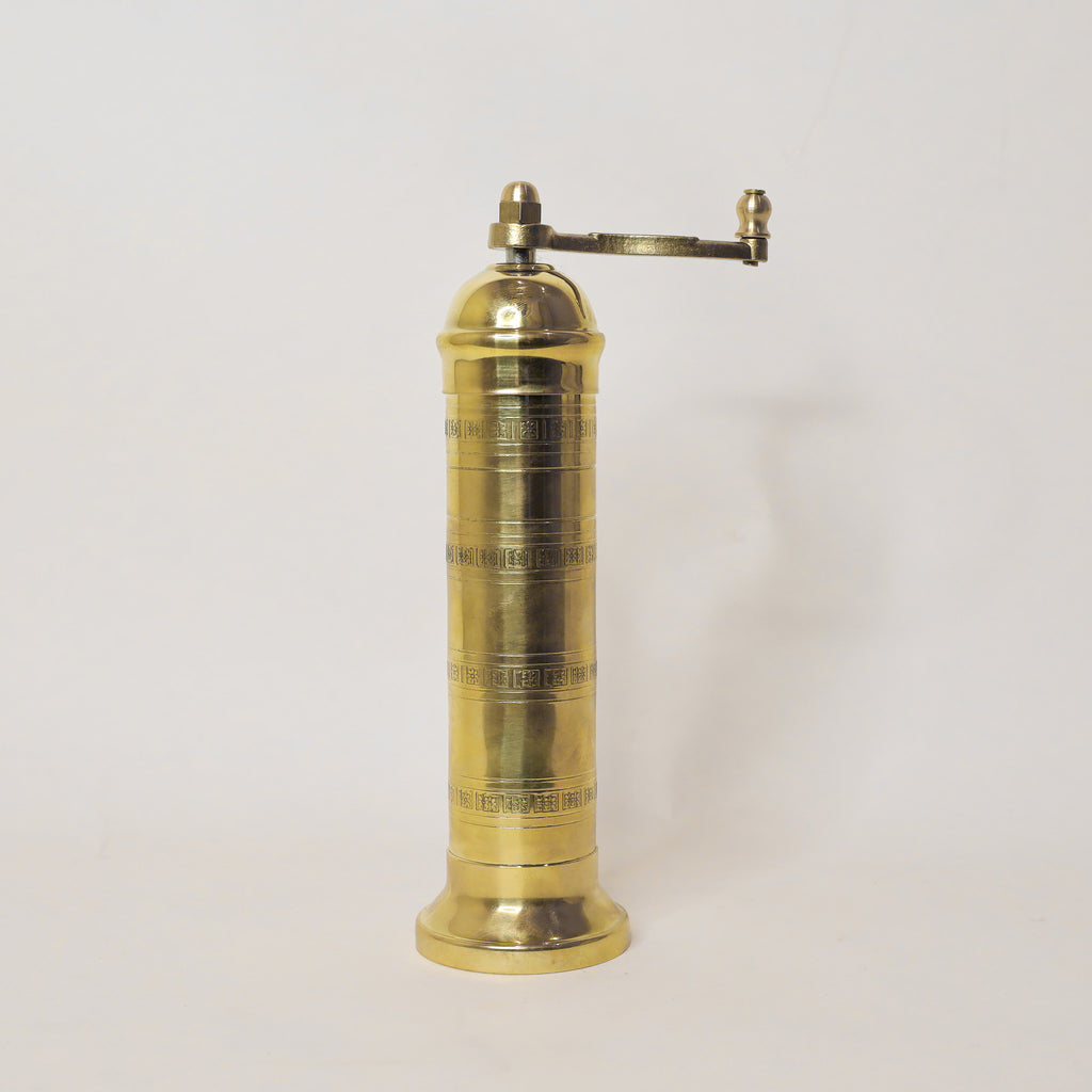 Brass pepper grinder on a light gray background