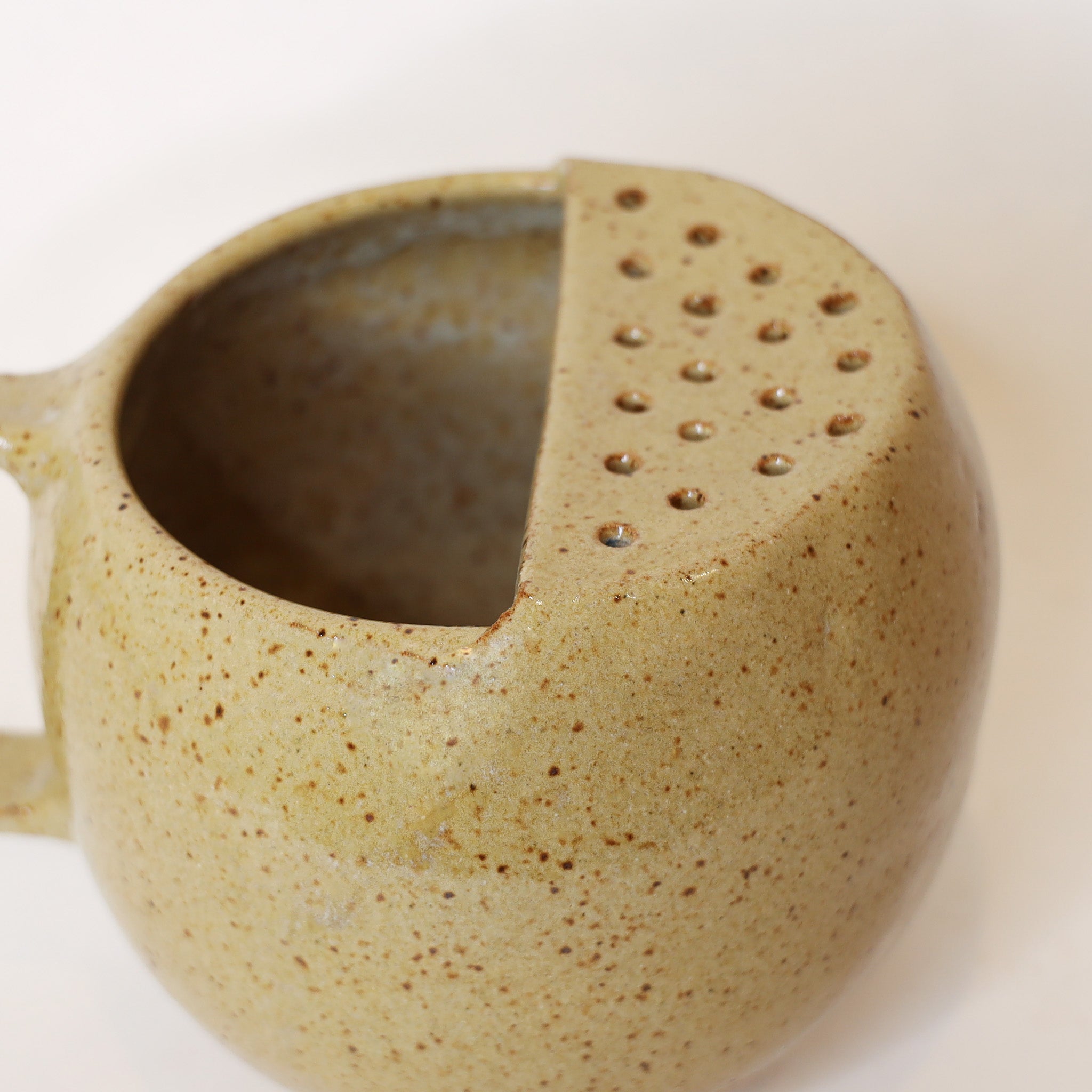 Speckled ceramic pitcher with a perforated spout on a white background