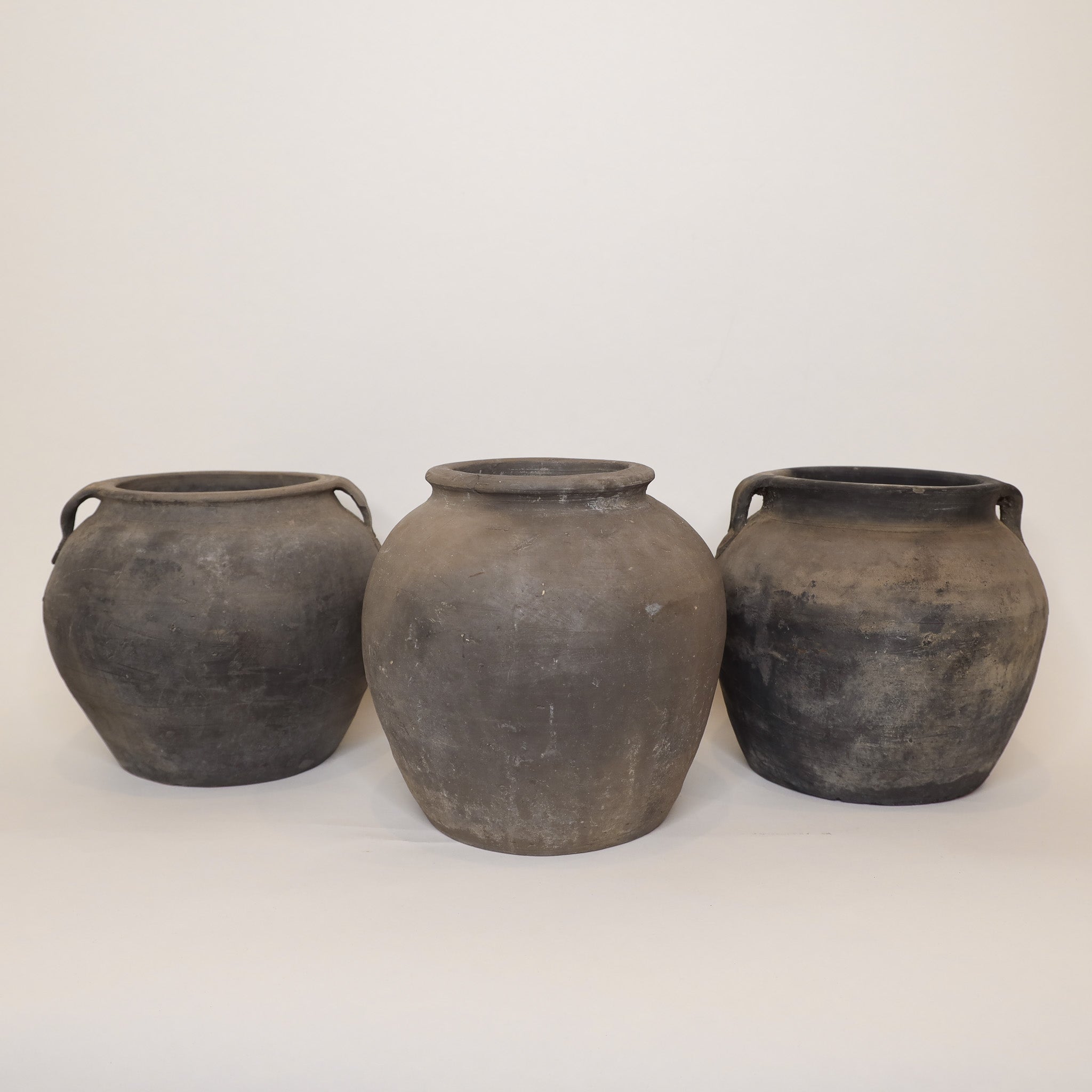 Three dark gray ceramic pots with handles on a white background