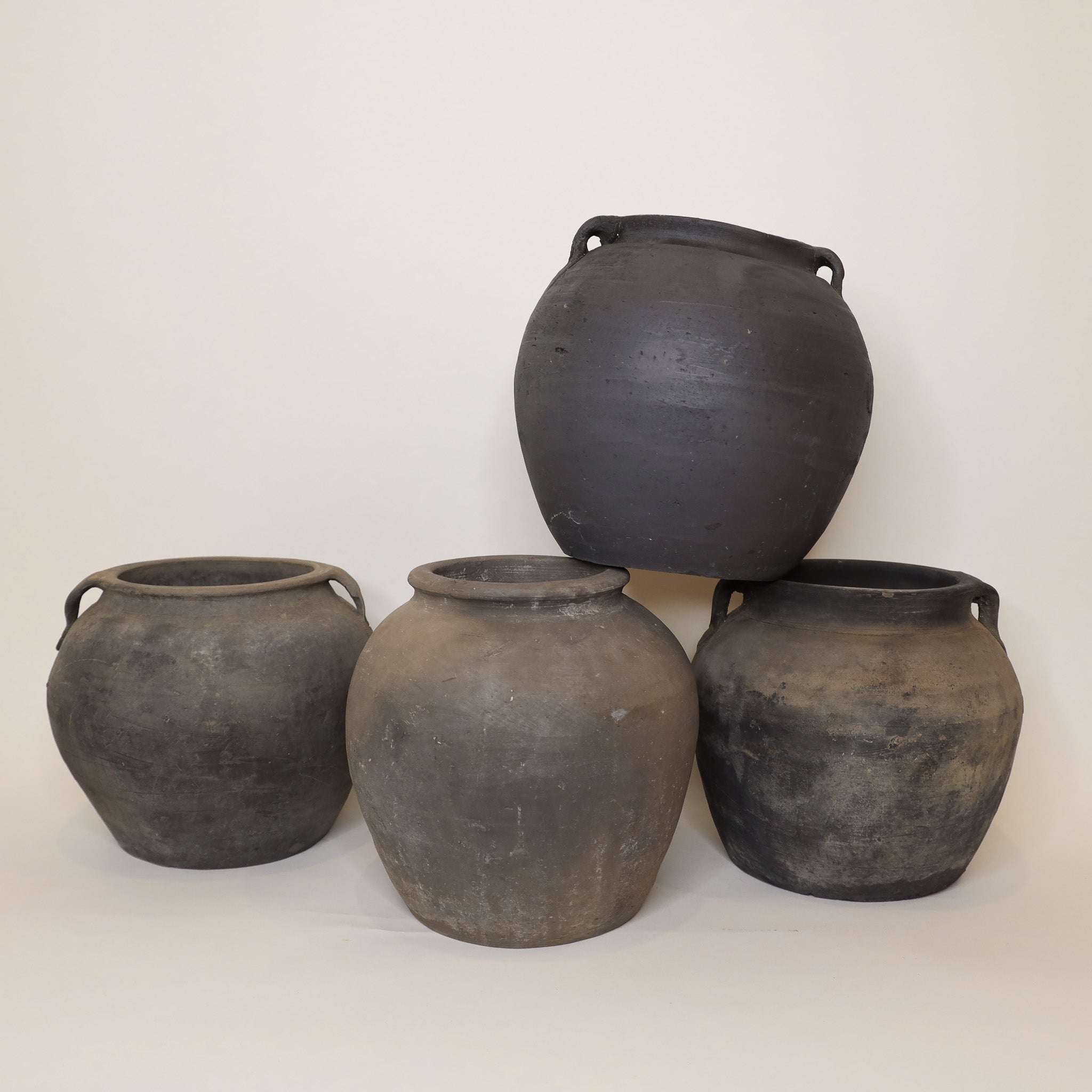 Four dark gray earthenware pots stacked on a white background