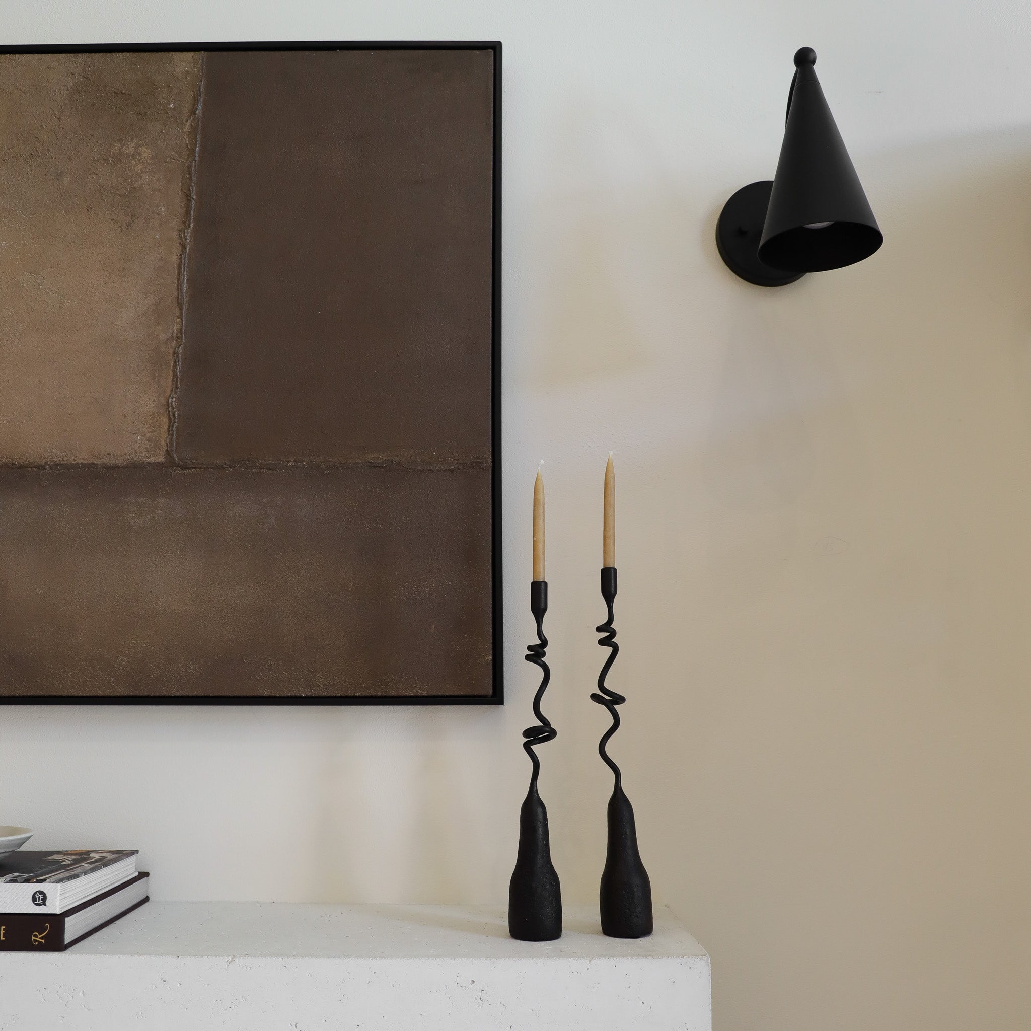 Black wall sconce and candle holders on a white surface with a neutral background