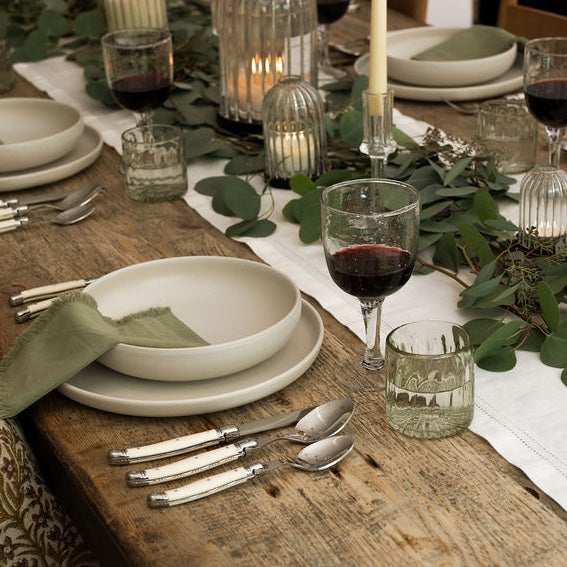 Elegant dinner table setting with white plates, silverware, glasses, and candles on a wooden table.