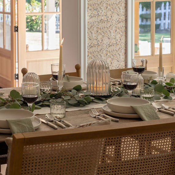 Elegant dining table setting with wine glasses, candles, and place settings in a bright room.