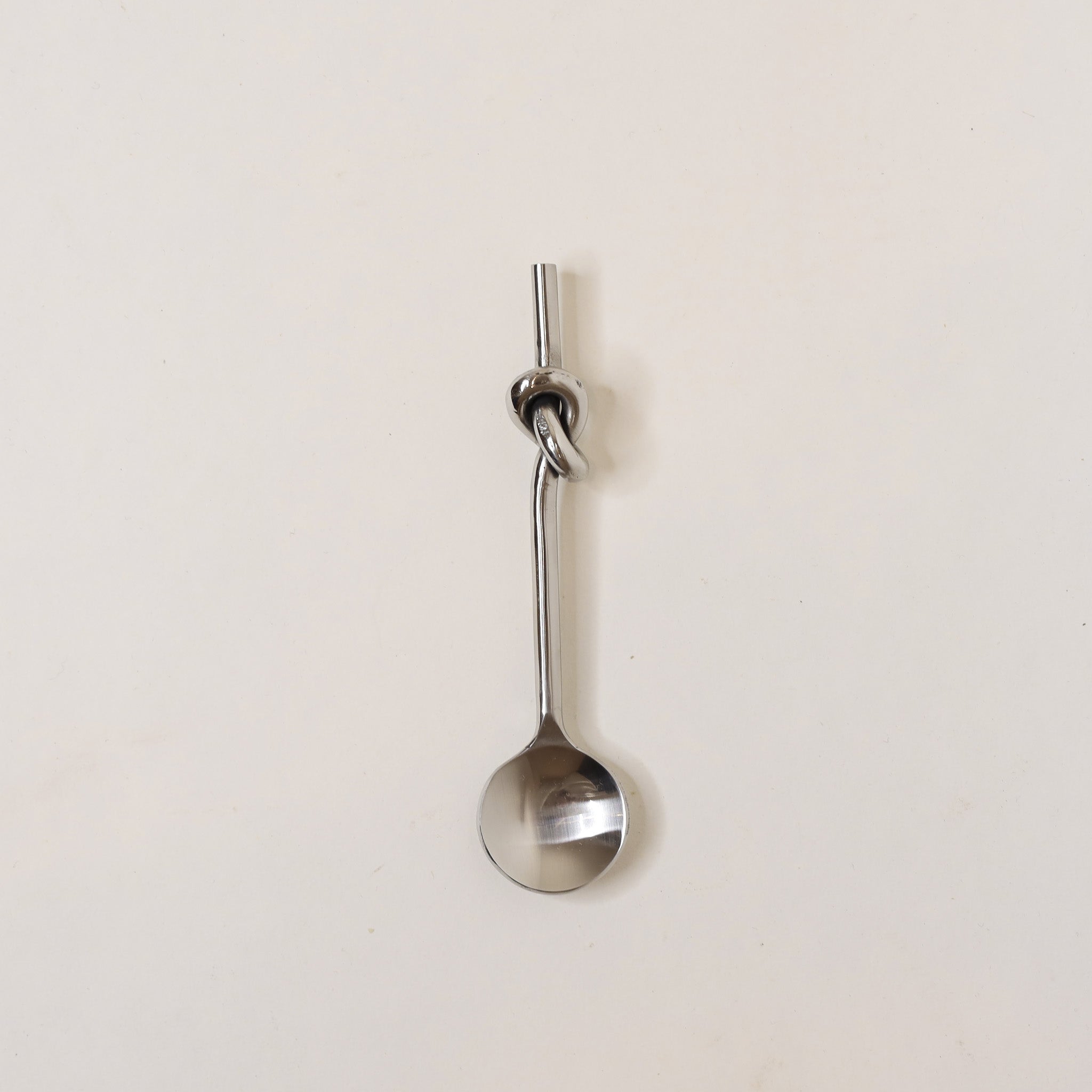 Metallic spoon with a knot on a light beige background