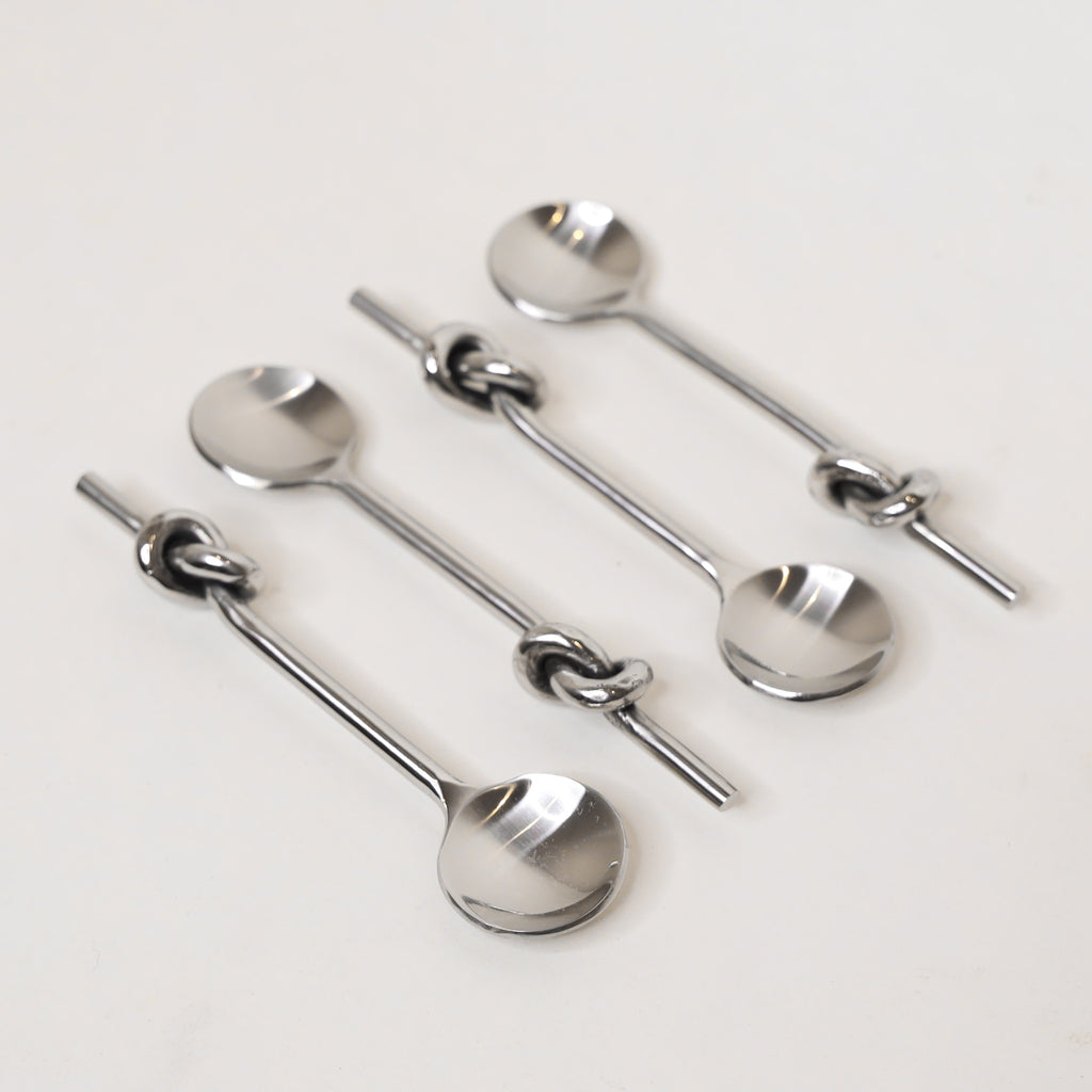 Set of four silver spoons with knot designs on a light gray background