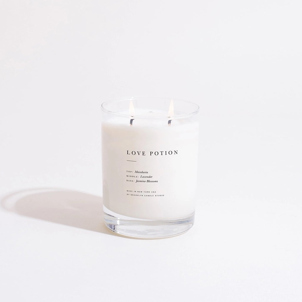 Candle in a glass jar labeled 'Love Potion' on a white background