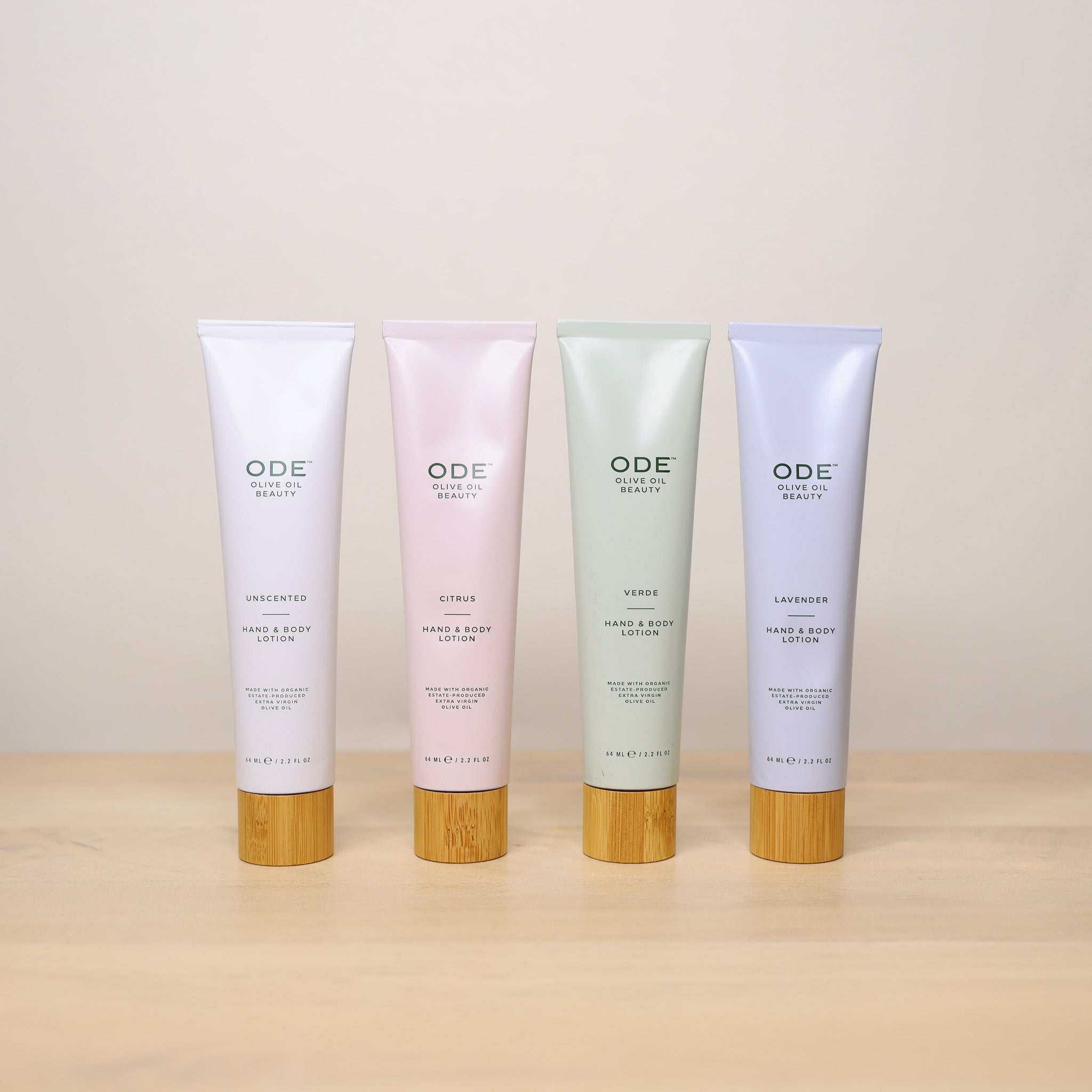 Four ODE Beauty hand and body lotions on a wooden surface with a beige background