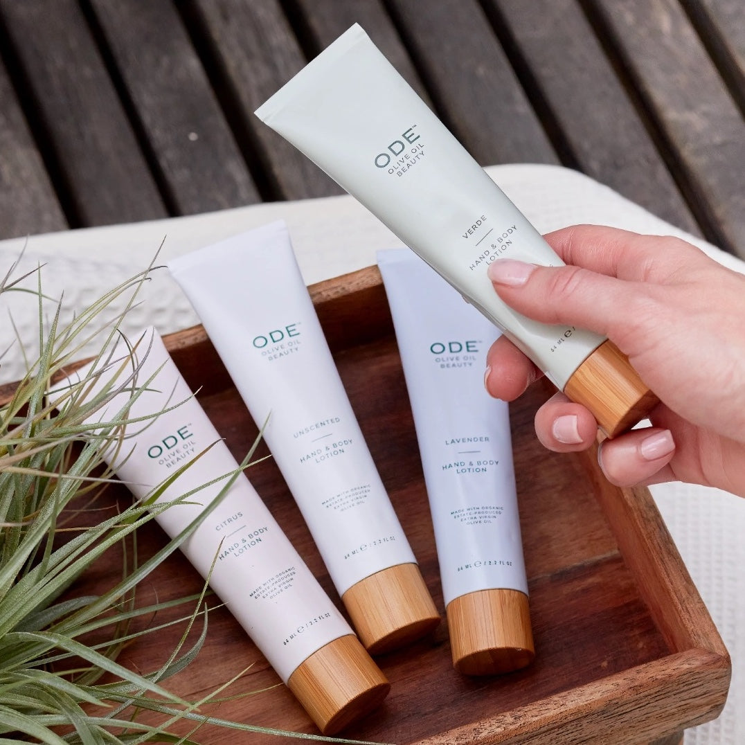 Hand holding an ODE Skincare product with other skincare items on a wooden tray.