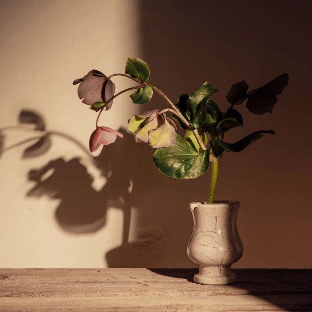 Vase with flowers on a wooden surface against a plain wall