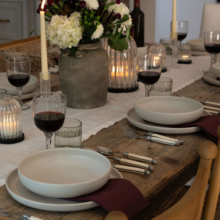 Dining table set with white plates, red wine, and floral centerpiece.