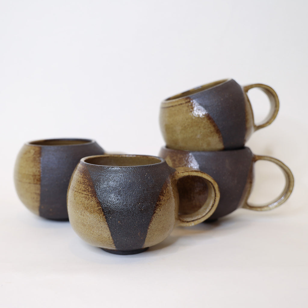 Four ceramic mugs with brown and black glaze on a white background