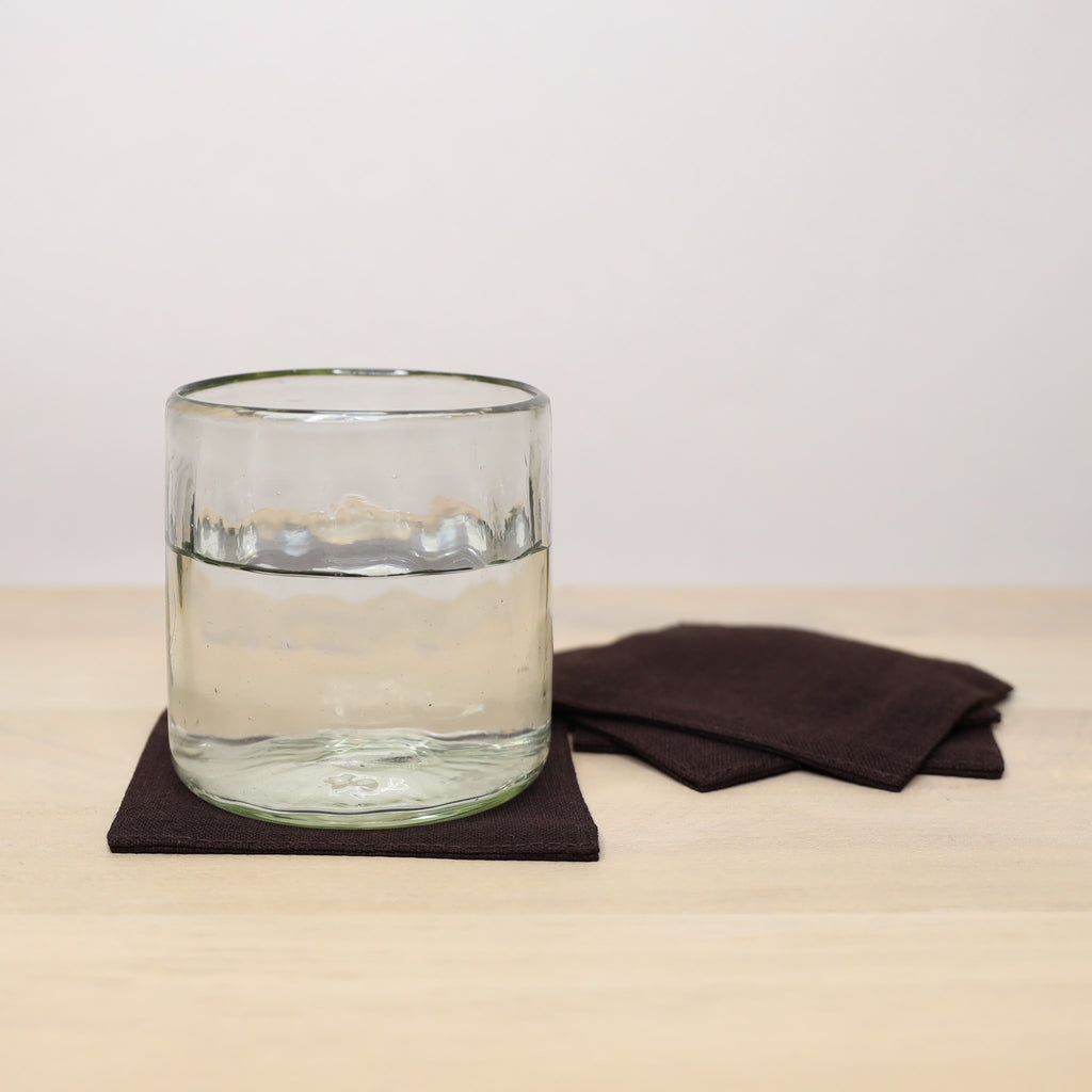 Clear glass of water on a dark coaster with a brown napkin on a beige surface.