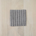Textured square mat with black stripes on a light wood surface