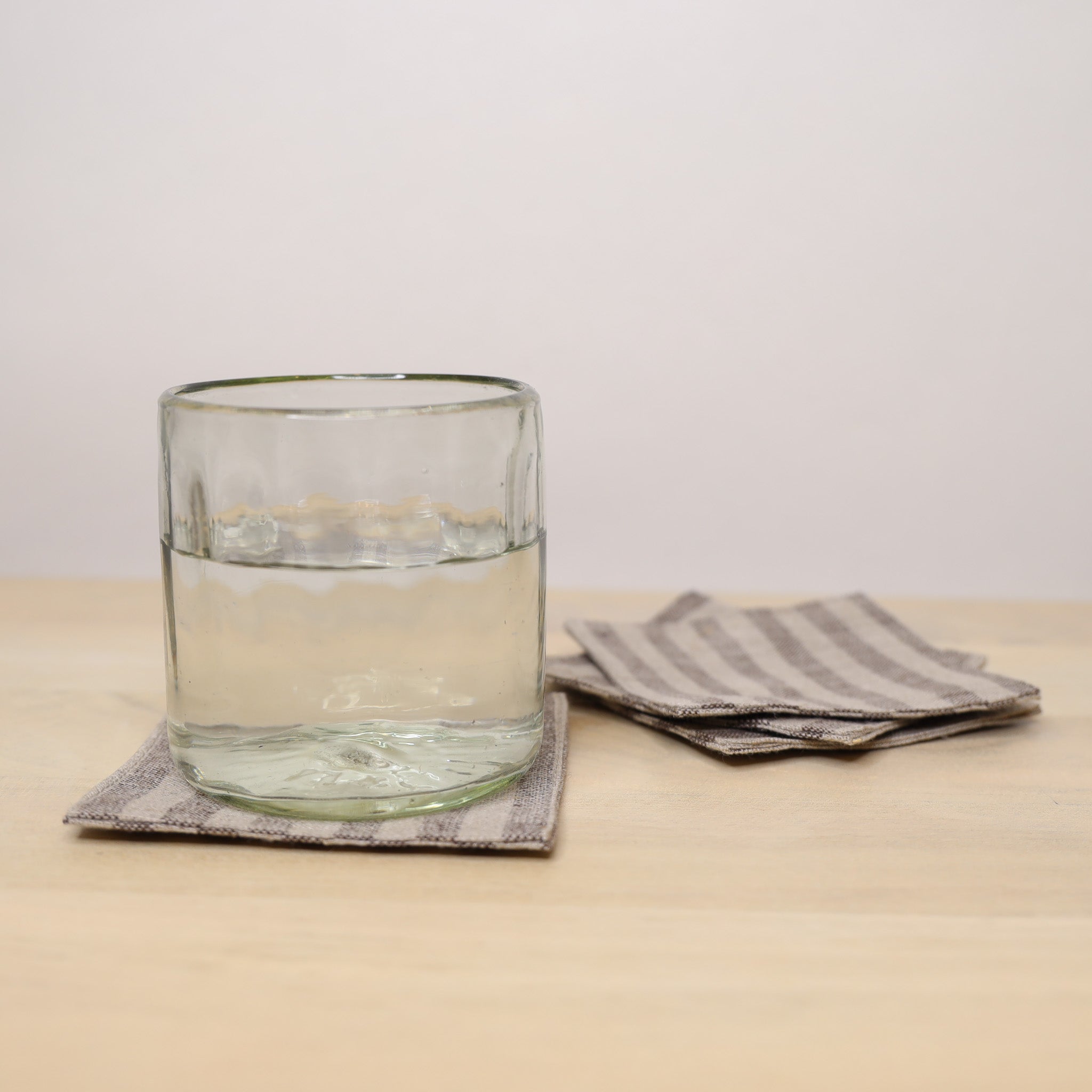 Clear glass of water on a coaster with a striped napkin on a wooden surface