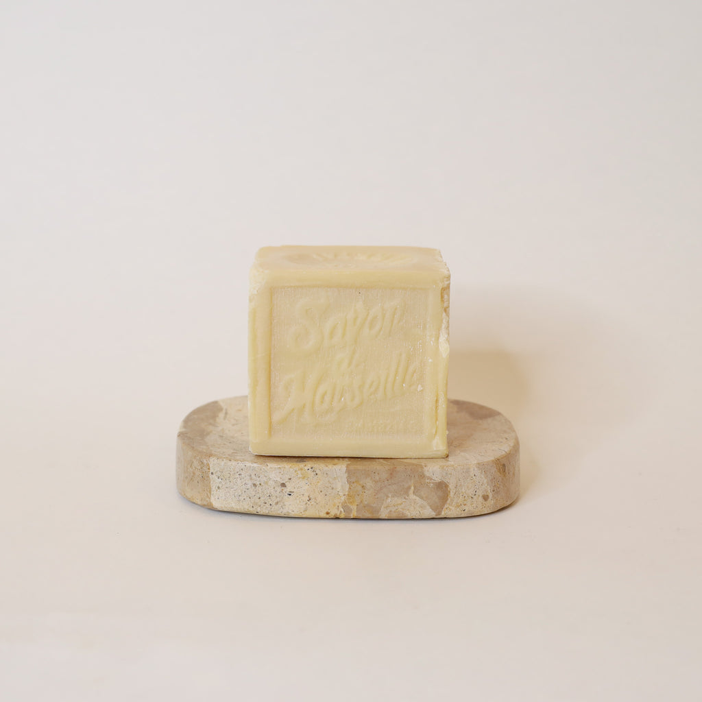 Square bar of soap on a round stone platform with a plain background