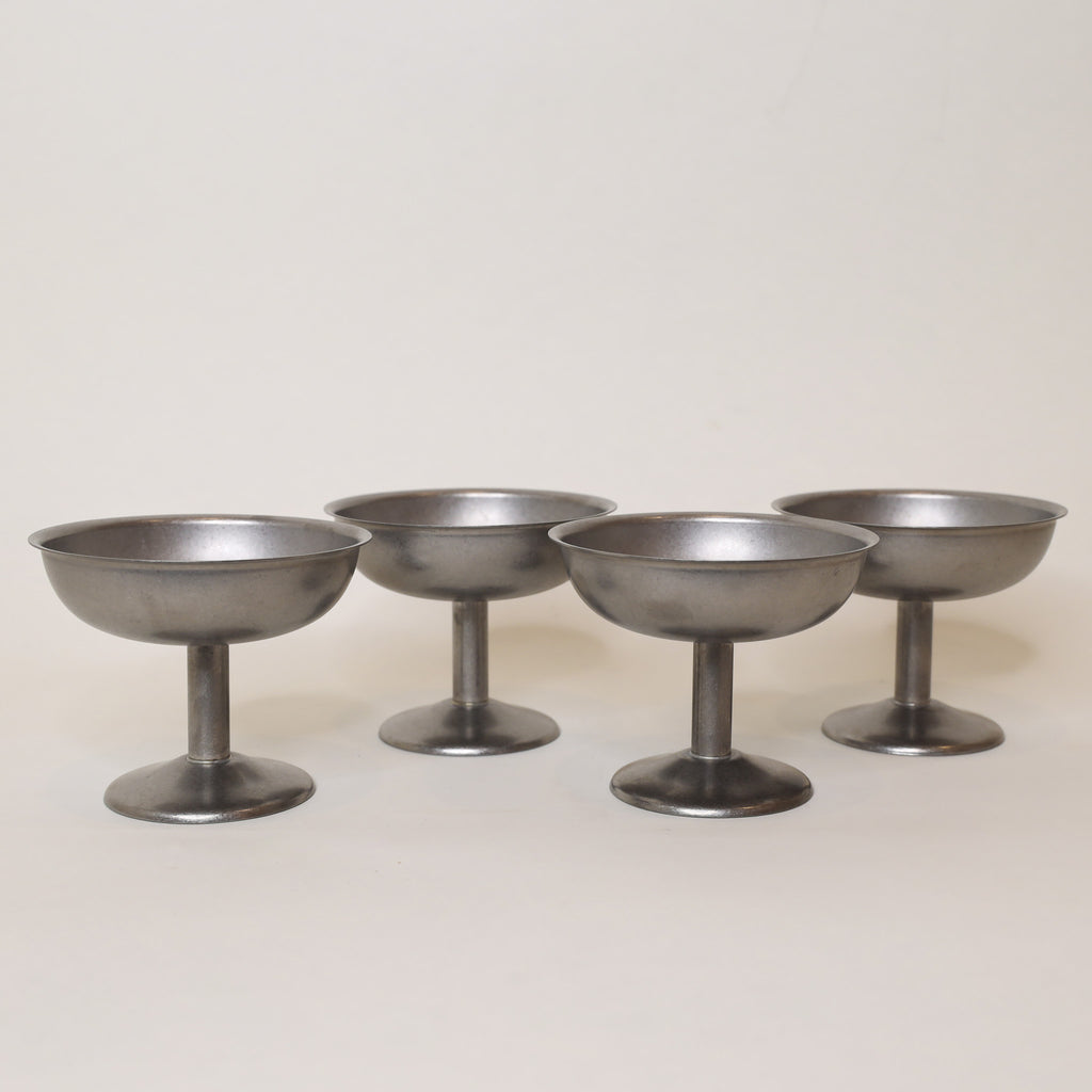 Four metallic cocktail coupes on a light gray background