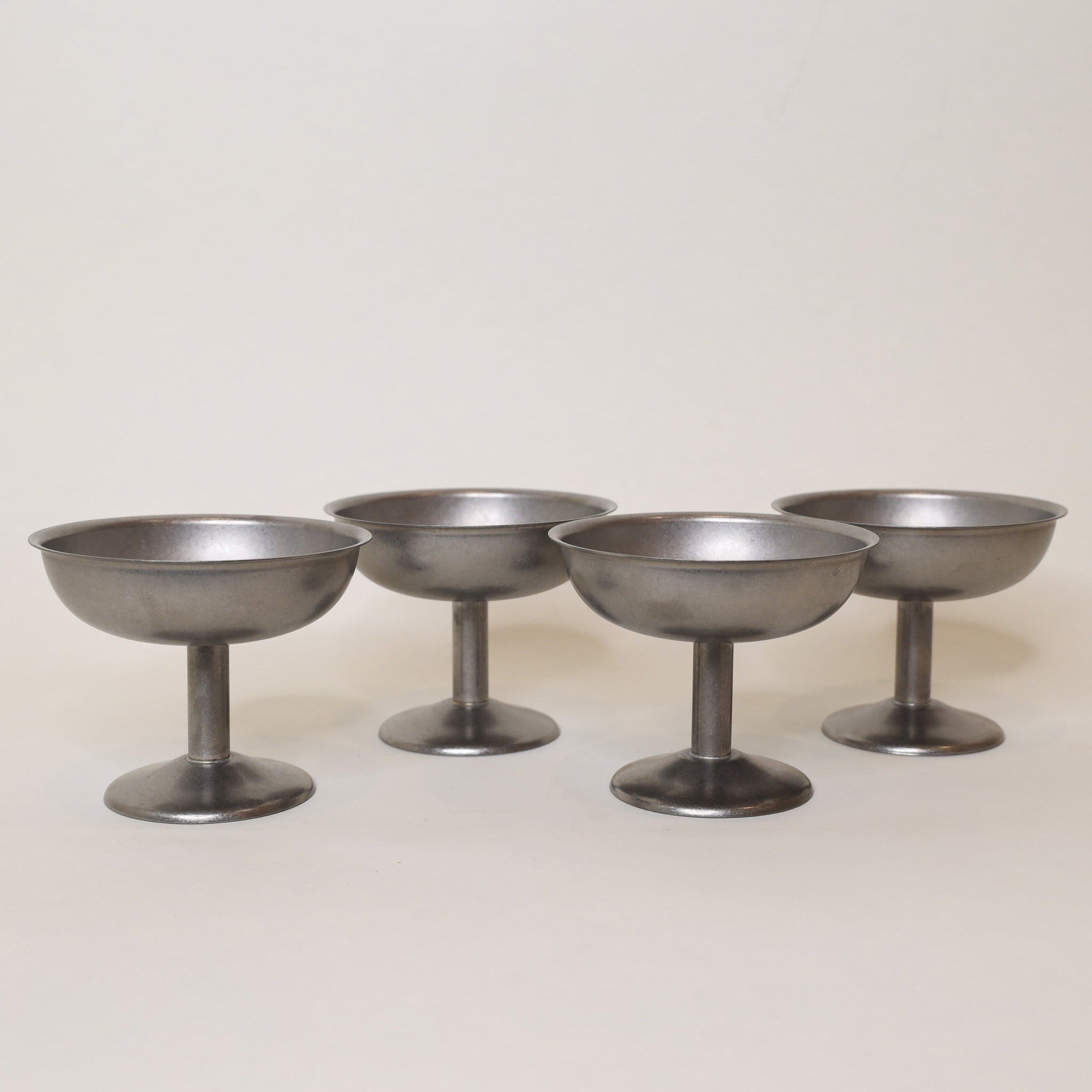 Four metallic cocktail coupes on a light gray background