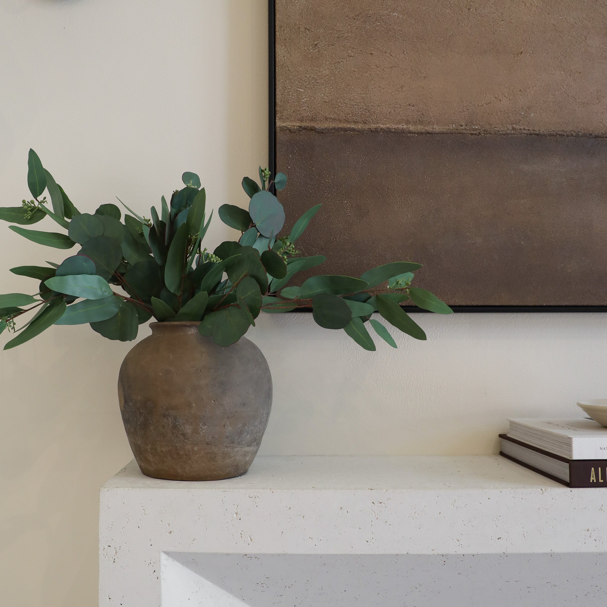 Vase with green leaves on a white surface with a neutral background